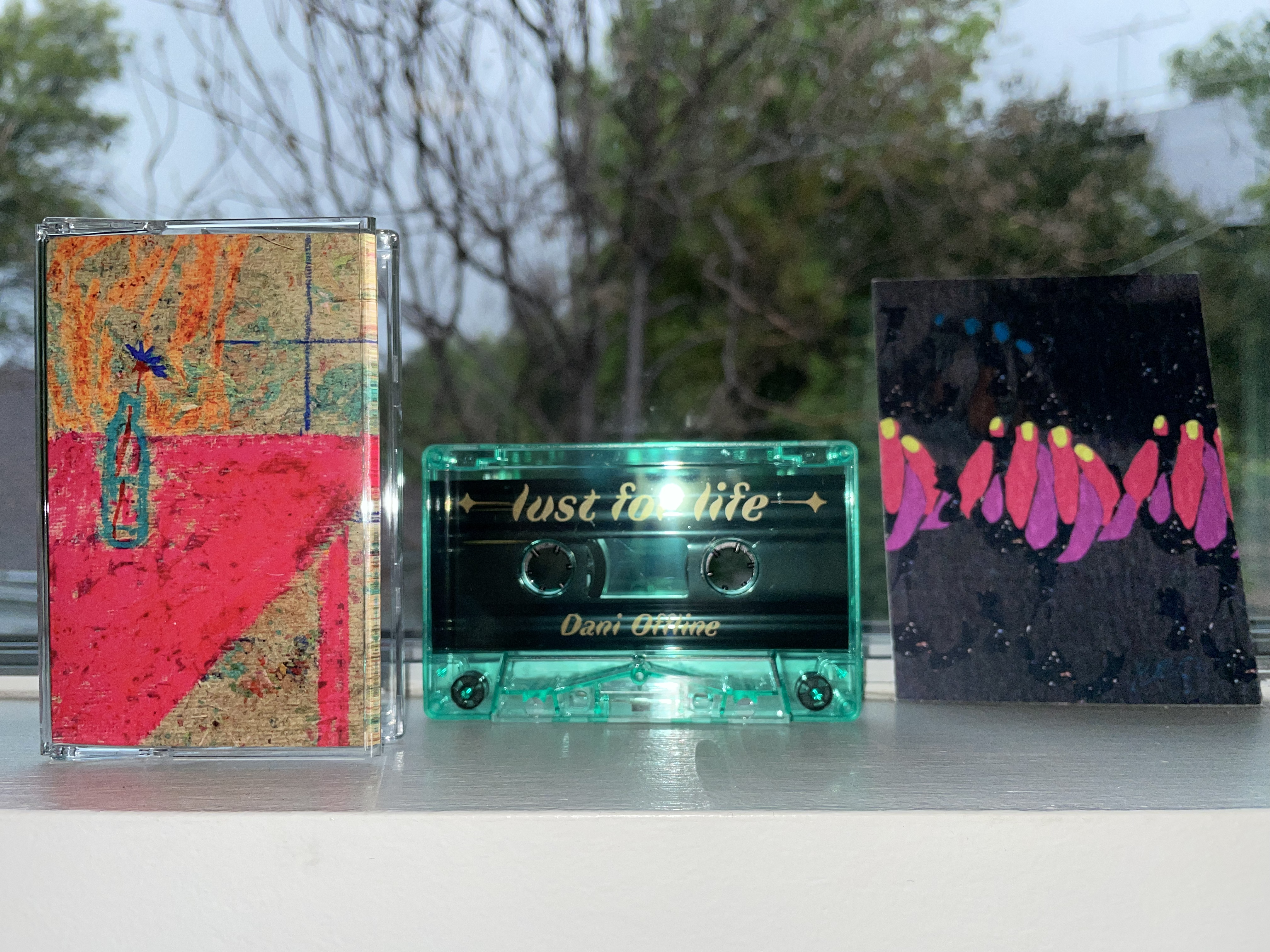 a cassette cover with a drawing of a bottle of flowers on a neon pink table, a green cassette tape, and a card with a drawing of hands holding